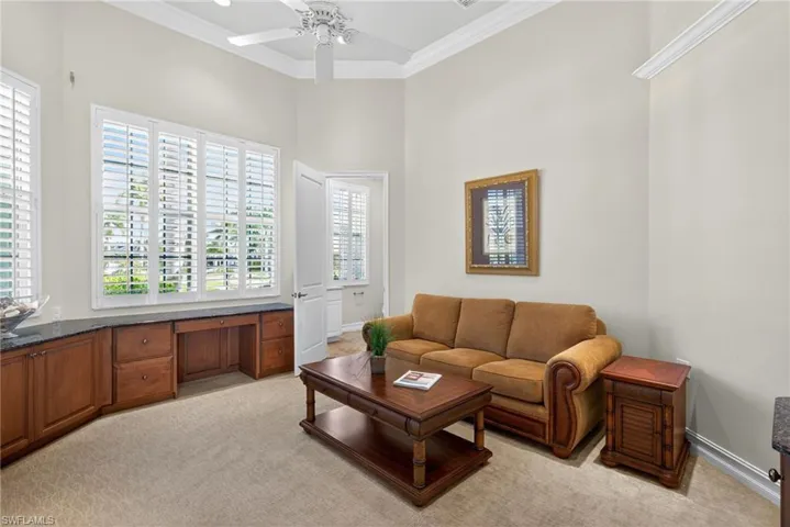 Living area with ornamental molding, light carpet, a ceiling fan, and a high ceiling