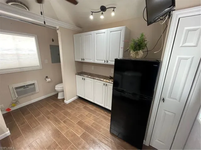 Kitchen with refrigerator, a wall mounted AC, electric panel, white cabinetry, and light wood-style flooring
