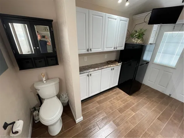 Kitchen featuring fridge, white cabinetry, light stone counters, and light wood-type flooring