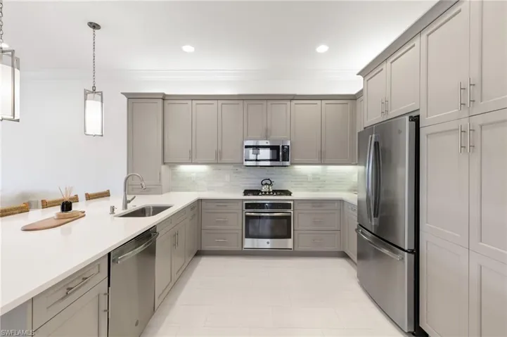 Kitchen with gray cabinetry, hanging light fixtures, stainless steel appliances, ornamental molding, and a peninsula