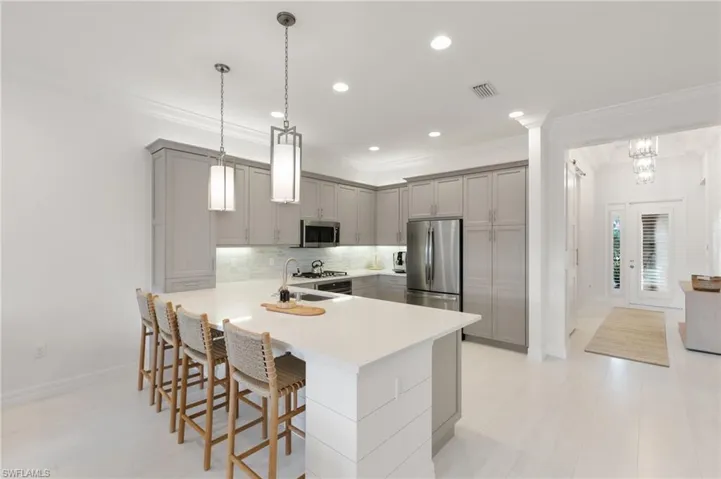 Kitchen with gray cabinetry, stainless steel appliances, decorative backsplash, hanging light fixtures, and a kitchen breakfast bar