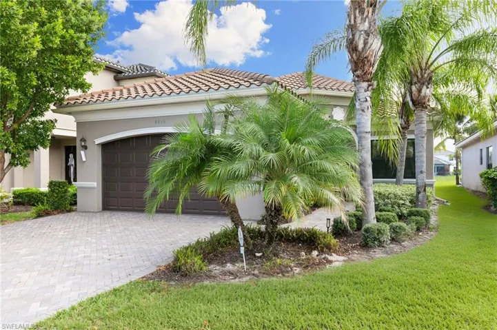 View of front of property featuring a tile roof, stucco siding, an attached garage, a front yard, and decorative driveway