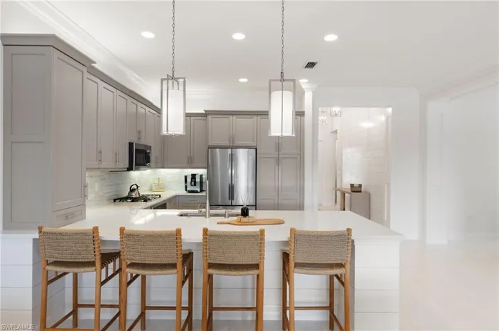Kitchen featuring gray cabinetry, a kitchen breakfast bar, decorative backsplash, hanging light fixtures, and ornamental molding