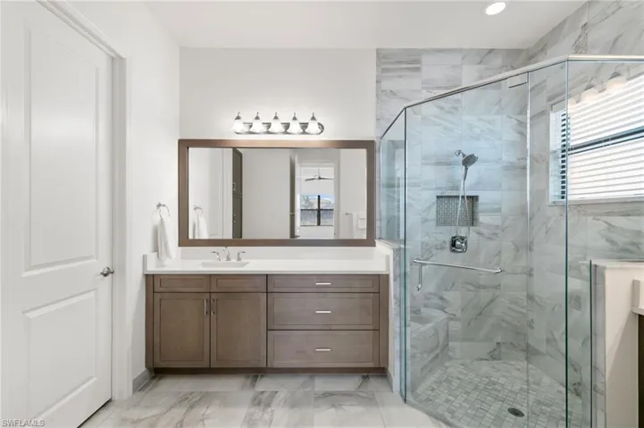 Full bath with vanity, healthy amount of natural light, a marble finish shower, and light marble finish floors