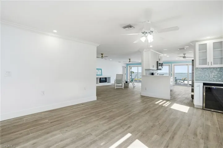 Living area with a fireplace, beverage cooler, recessed lighting, crown molding, and light wood finished floors - Virtually Edited Image