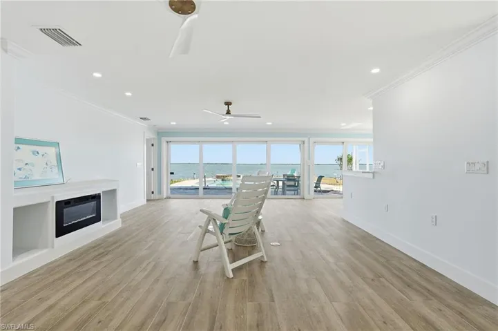 Living area featuring a water view, a glass covered fireplace, healthy amount of natural light, light wood-style floors, and ornamental molding - Virtually Edited Image