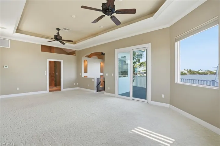 Empty room featuring a tray ceiling, crown molding, light colored carpet, and ceiling fan - Virtually Edited Image