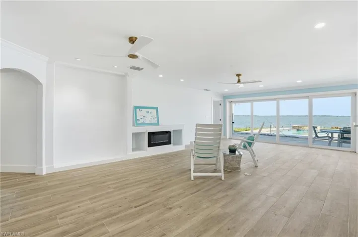 Living room featuring a water view, crown molding, a glass covered fireplace, light wood-style floors, and a ceiling fan - Virtually Edited Image