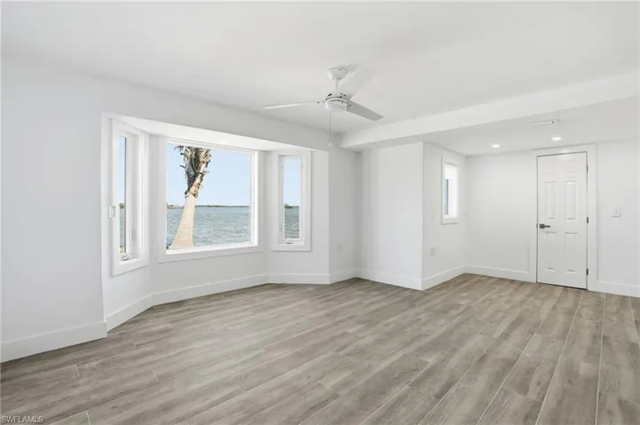 Empty room with light wood finished floors, ceiling fan, recessed lighting, and a water view - Virtually Edited Image