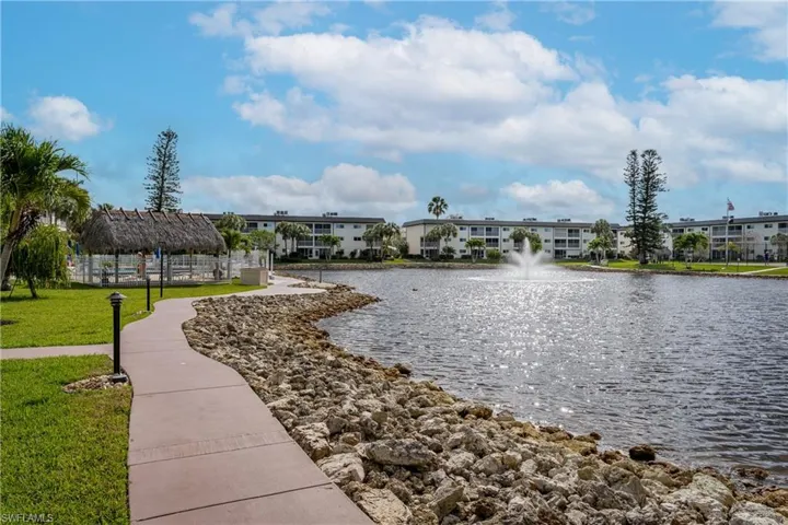 Waterfront property featuring a fountain, rock-lined shore, and manicured landscaping