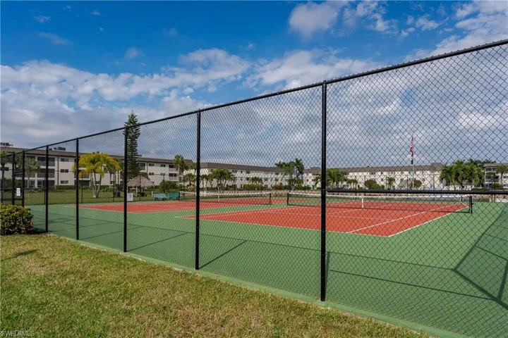 Dual tennis courts featuring green and red playing surfaces, enclosed by black chain-link fencing