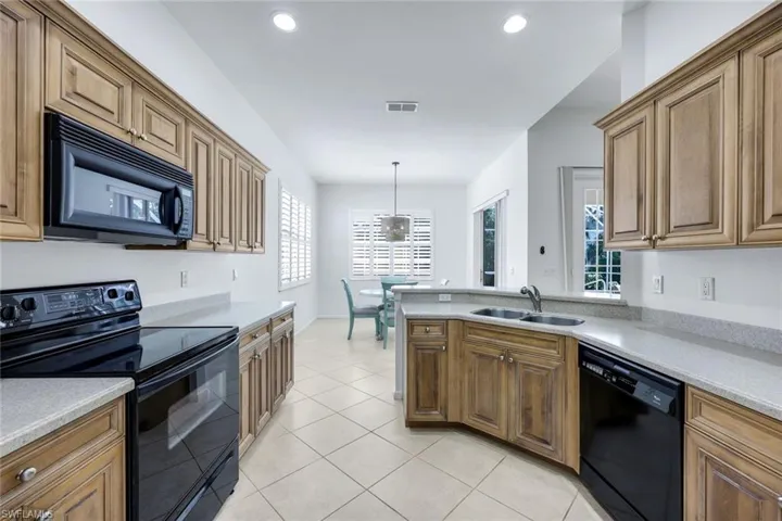 Kitchen with light tile patterned floors, brown cabinets, light countertops, black appliances, and a sink