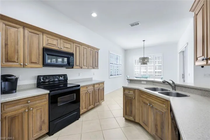 Kitchen featuring light tile patterned floors, visible vents, hanging light fixtures, light countertops, and black appliances