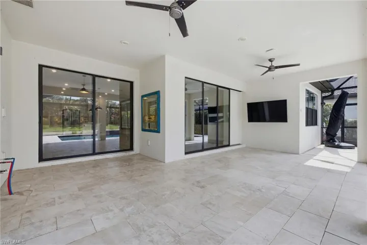 Spacious outdoor living area with light-toned rectangular tile flooring, multiple sliding glass doors, and two ceiling fans