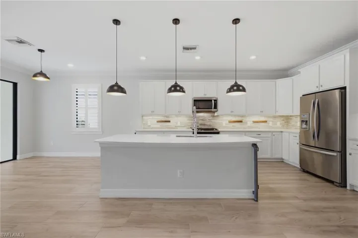 Kitchen featuring a large island with sink, white shaker cabinetry, stainless steel appliances, and wood-finish flooring