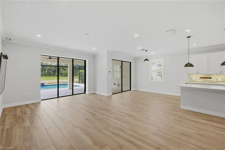 Expansive main living area featuring wood-finish flooring, a kitchen island with stone countertop, white shaker cabinetry, recessed lighting, and sliding glass doors opening to a screened patio with a pool