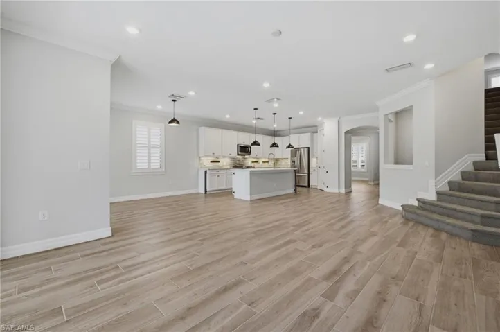 Open-concept living space featuring wood-finish flooring, recessed lighting, and a modern kitchen with white cabinetry and an island