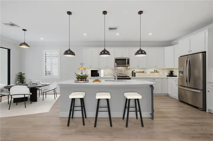 Modern kitchen featuring a large island with seating, stainless steel appliances, white cabinetry, wood-finish flooring, and pendant lighting