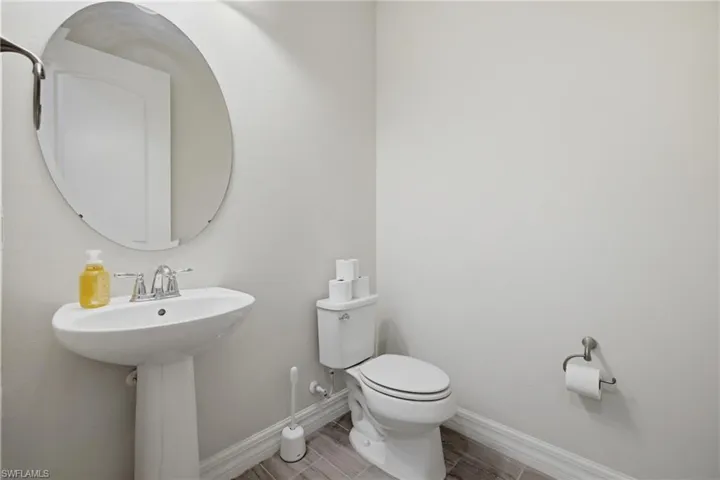 Pedestal sink with chrome faucet, oval mirror, and wood-finish tile flooring