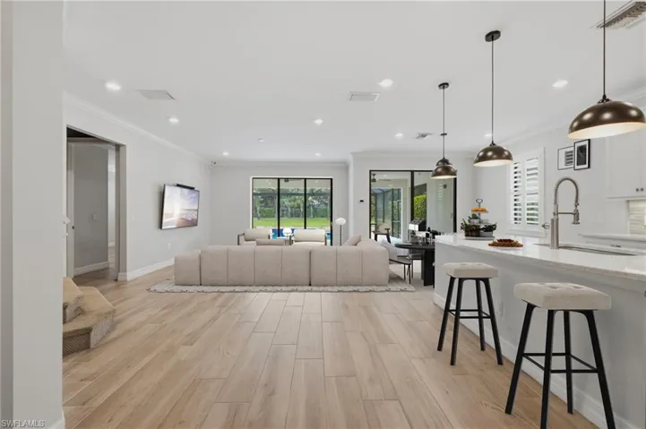 Open-concept living area featuring light wood-finish flooring, recessed lighting, and crown molding