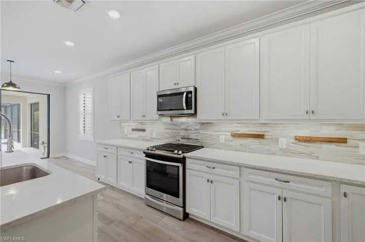 Modern kitchen featuring white shaker cabinetry, stainless steel appliances, light-toned countertops, a light-toned tile backsplash, and recessed lighting