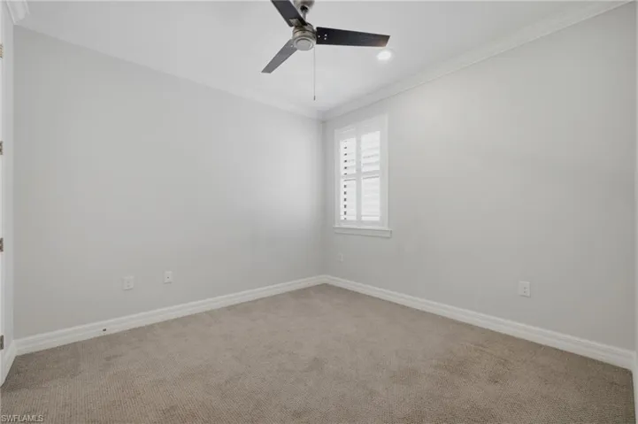 Carpeted room featuring a ceiling fan with integrated lighting, a window with plantation shutters, crown molding, and baseboards