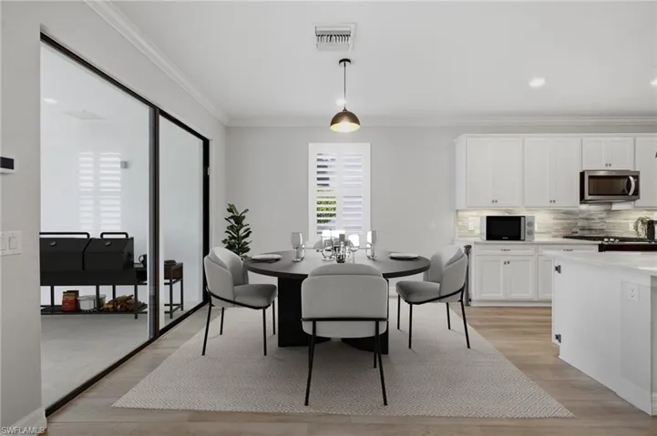 Open-concept dining area featuring wood-finish flooring, a contemporary pendant light fixture, and crown molding
