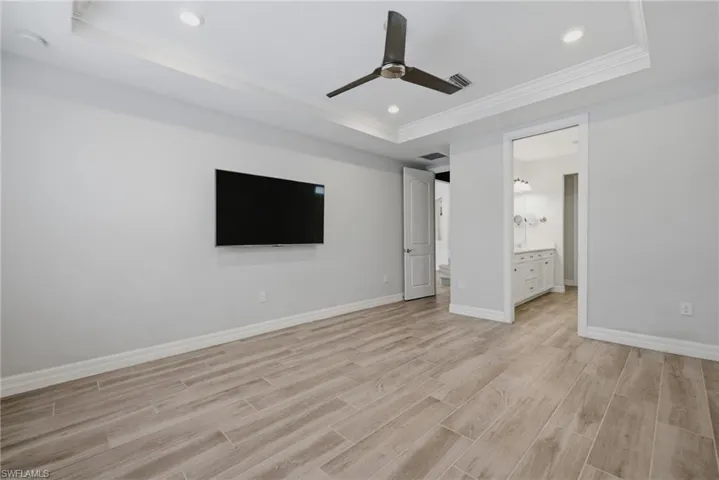 Spacious room featuring wood-finish flooring, a tray ceiling with recessed lighting, and a dark-toned ceiling fan