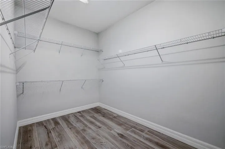 Spacious closet featuring wood-finish flooring, white baseboards, light gray walls, and wire shelving