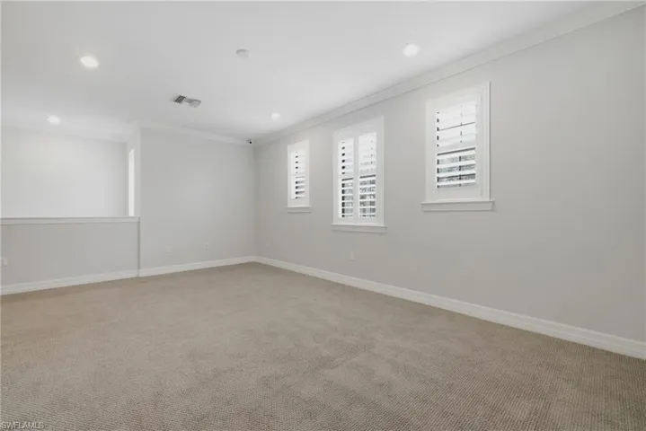 Carpeted room featuring white plantation shutters, recessed lighting, and crown molding