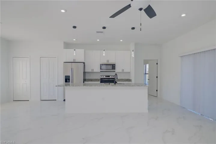 Kitchen with a center island with sink, white cabinetry, pendant lighting, and appliances with stainless steel finishes