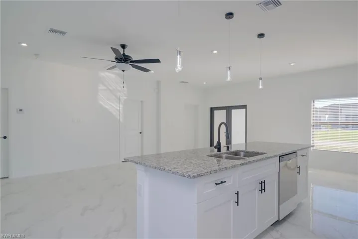 Kitchen with sink, white cabinets, a kitchen island with sink, stainless steel dishwasher, and pendant lighting