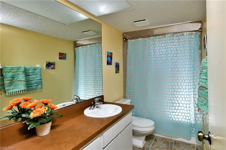 Full bathroom with vanity, shower / bath combo with shower curtain, toilet, and a textured ceiling