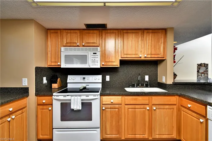 Kitchen featuring a textured ceiling, white appliances, sink, and tasteful backsplash