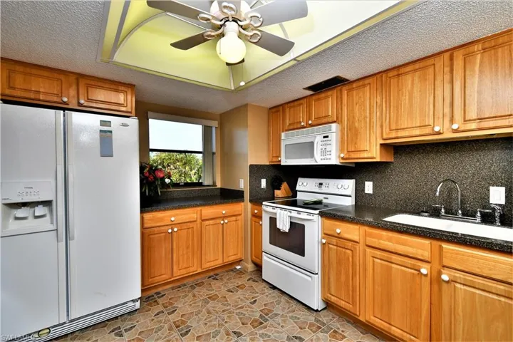 Kitchen featuring ceiling fan, sink, white appliances, tasteful backsplash, and a textured ceiling