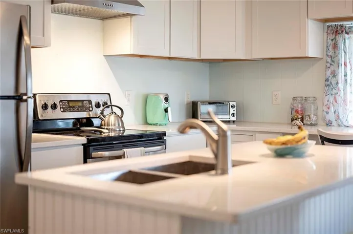 Kitchen featuring light countertops, wall chimney range hood, a toaster, and appliances with stainless steel finishes
