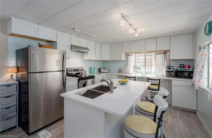 Kitchen with light wood finished floors, under cabinet range hood, a sink, and stainless steel appliances