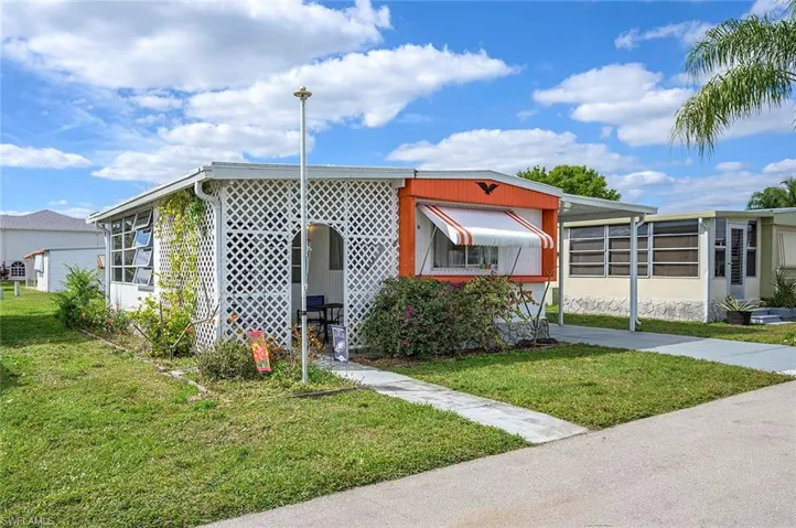 Manufactured / mobile home featuring a front lawn, driveway, and a carport