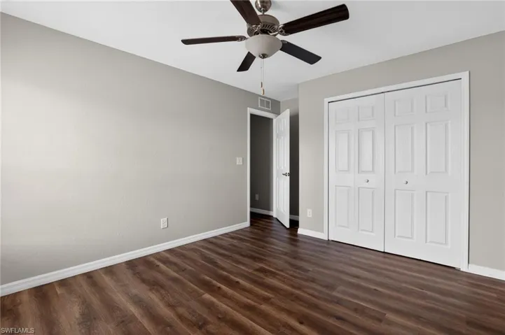 Spacious room featuring wood-finish flooring, light grey walls, white baseboards, and a ceiling fan with integrated lighting