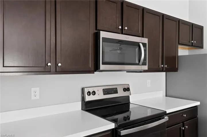Kitchen featuring dark wood-finish cabinetry, white countertops, stainless steel microwave, and a black electric range with stainless steel accents
