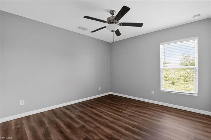Spacious room featuring wood-finish flooring, light gray walls, white baseboards, and a ceiling fan with light fixture