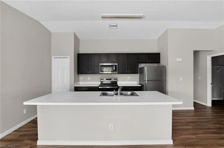 Open concept kitchen featuring an extended island with a dual basin sink, contrasting dark cabinetry, and stainless steel appliances