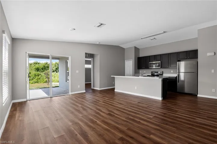 Open-concept living space featuring wood-finish flooring, a kitchen island with seating, dark wood cabinetry, stainless steel appliances, and sliding glass doors to an outdoor patio