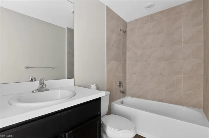 Bathroom featuring a white bathtub with a tiled surround, a toilet, a vanity with a white countertop and integrated sink, and a large wall mirror