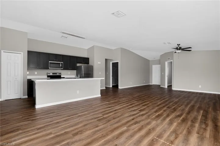 Open-concept living area featuring wood-finish flooring, a contemporary kitchen, vaulted ceilings, and a ceiling fan