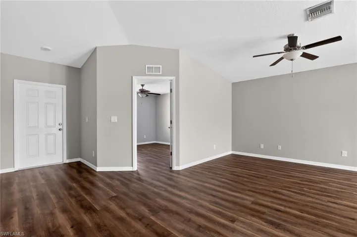Spacious room featuring wood-finish flooring, vaulted ceilings, and a ceiling fan with integrated lighting