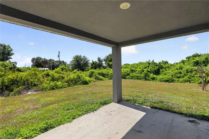 Covered patio with a concrete slab, recessed lighting, and a view of the expansive grassy area and surrounding lush foliage