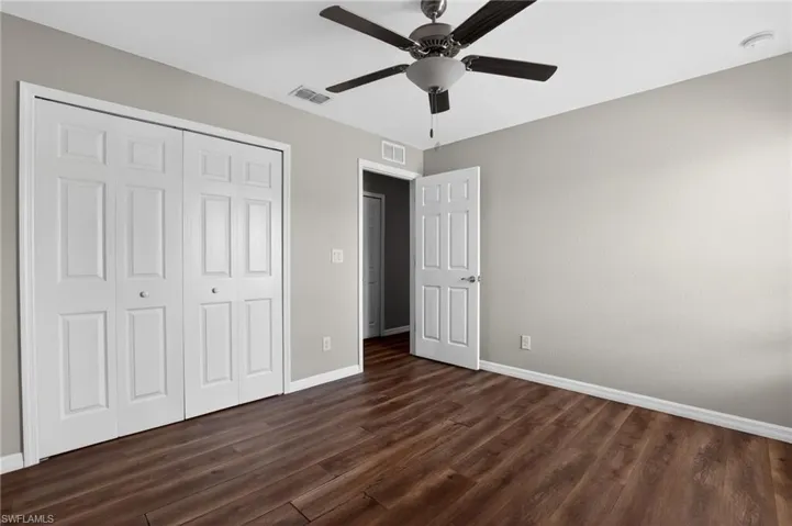Room featuring wood-finish flooring, light gray walls, a ceiling fan with integrated lighting, white baseboards, and a bi-fold closet with paneled doors