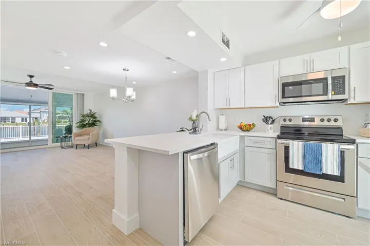 Kitchen featuring light hardwood / wood-style flooring, ceiling fan with notable chandelier, stainless steel appliances, kitchen peninsula, and white cabinetry
