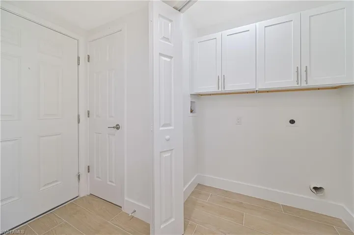 Laundry area with light hardwood / wood-style floors, hookup for an electric dryer, and cabinets